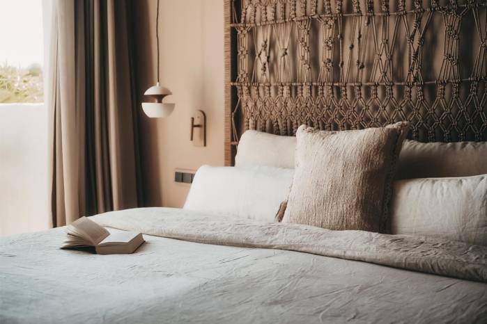 Acogedora cama con cabecero decorativo, almohadas y un libro en la Suite Lado Campo del Hotel Barefoot en Mallorca.