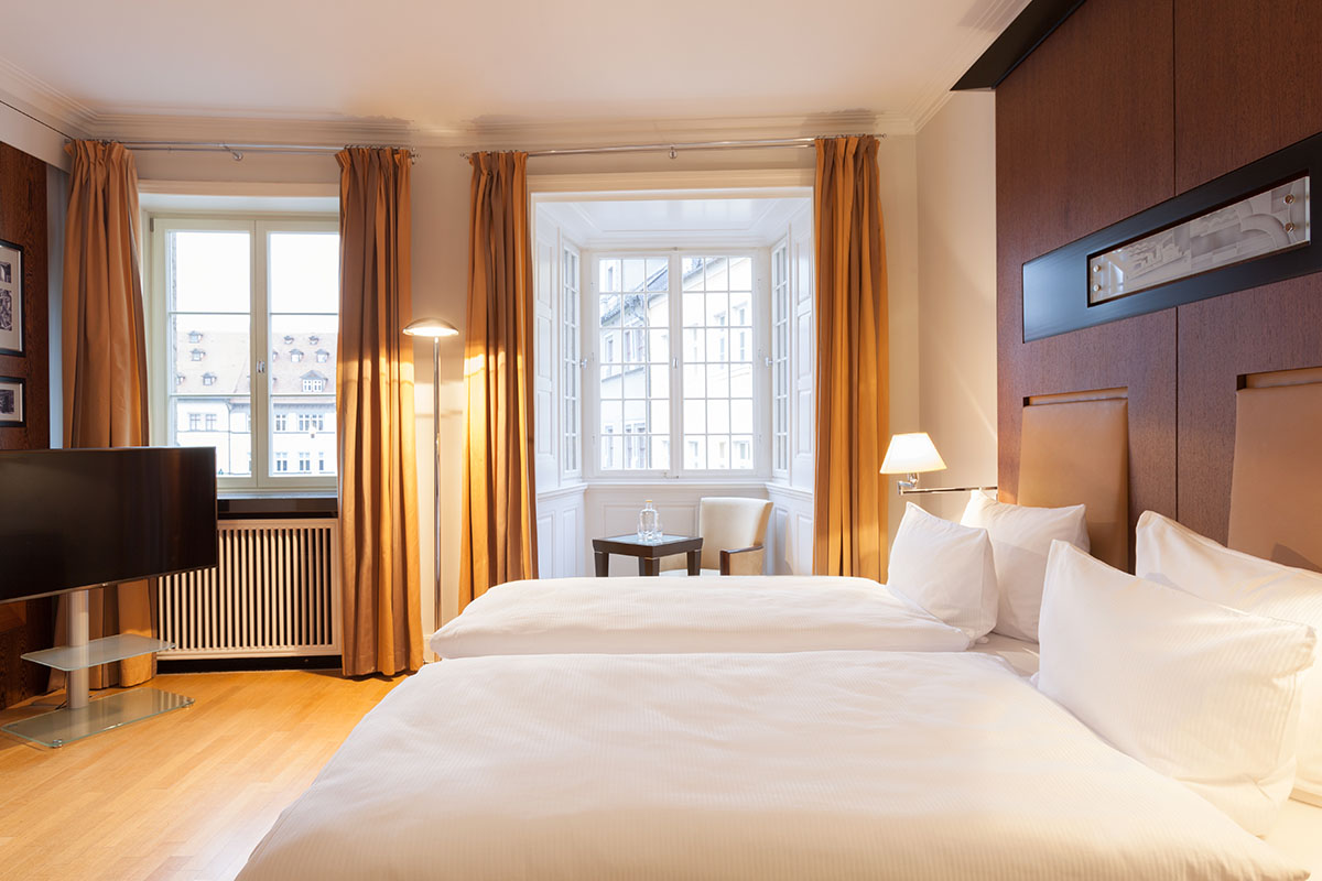 Schlafzimmer der Thomas Mann Suite im Hotel Elephant Weimar mit zwei luxuriösen Betten, warmem Licht und elegantem Design.