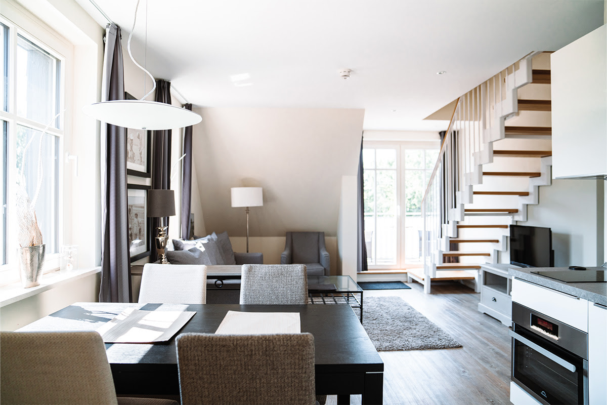 Bright living area with dining table, sofa and staircase in the Dünenpark vacation apartment, part of the Künstlerquartier Seezeichen hotel.