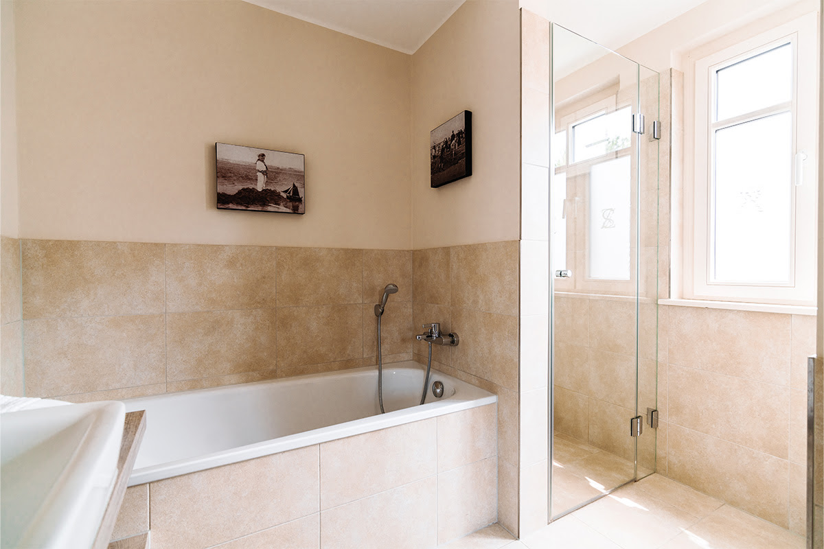 Spacious bathroom in the Seeipferd vacation apartment in the Hotel Künstlerquartier Seezeichen with bathtub and glass shower.