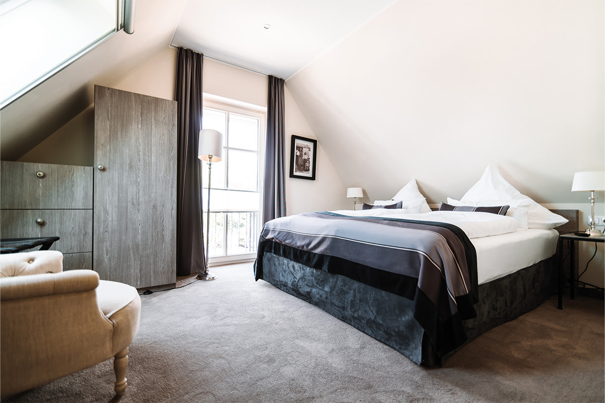 Bedroom of the Strandnixe vacation apartment with double bed, TV and plenty of natural light, part of the Künstlerquartier Seezeichen hotel.