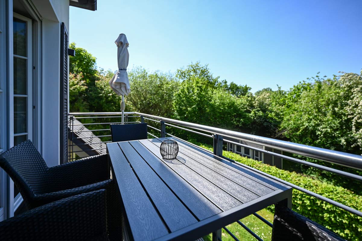 Balcony of the Seeadler vacation apartment in the Hotel Künstlerquartier Seezeichen with modern furniture and a view of the greenery.