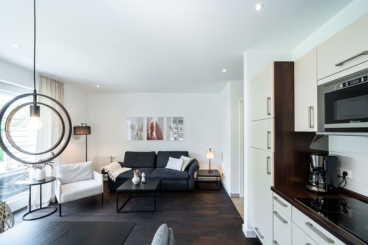 Bright living area with sofa, kitchenette and large windows in the Seeschwalbe vacation apartment in the Hotel Künstlerquartier Seezeichen.