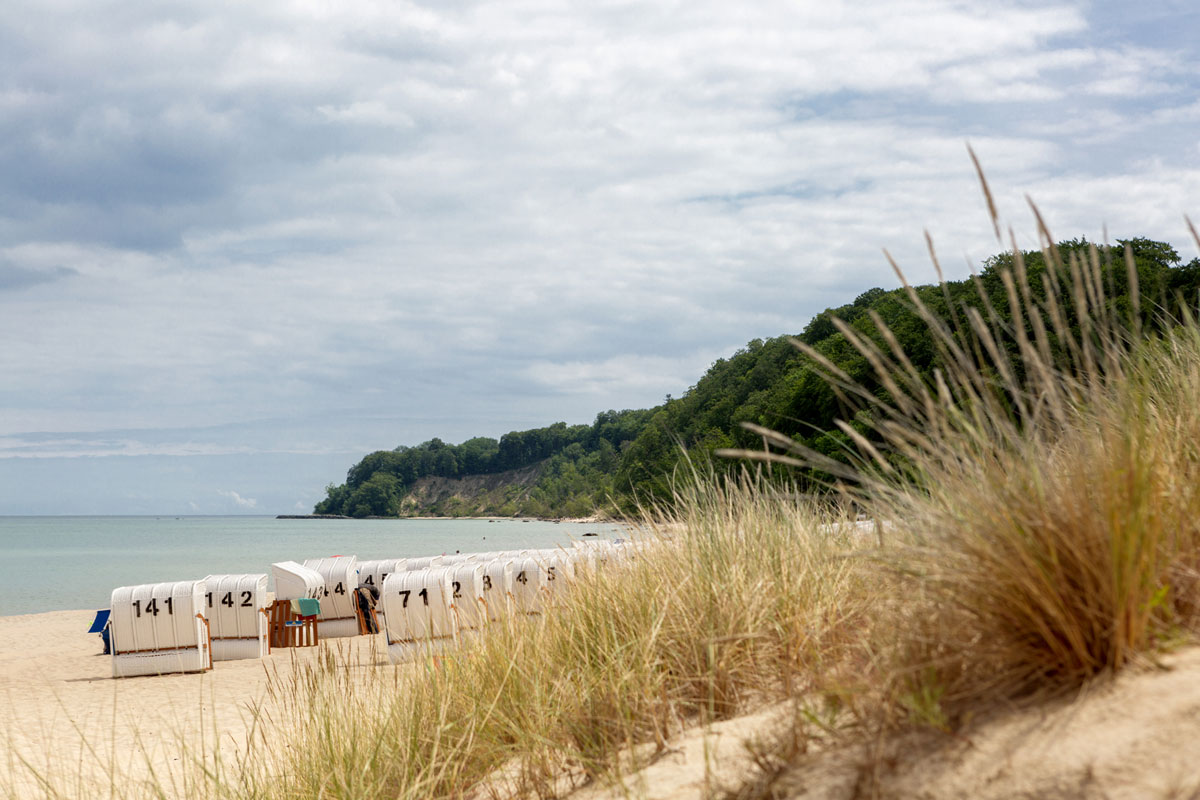 White sandy beach on Rügen with beach chairs and green dunes in front of picturesque cliffs on vacation at the Vju Hotel.
