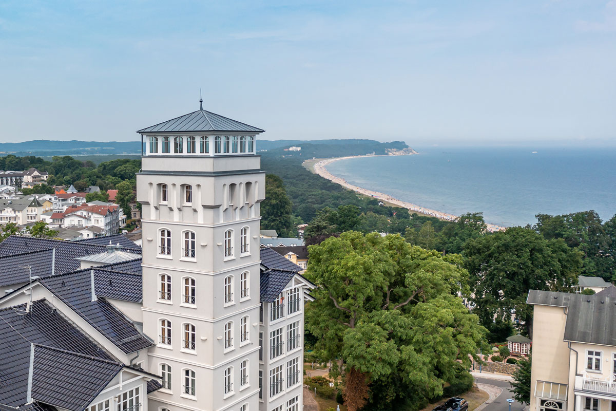 Exterior view of the Vju Hotel with its striking tower, white facades and view of the coast of Rügen.
