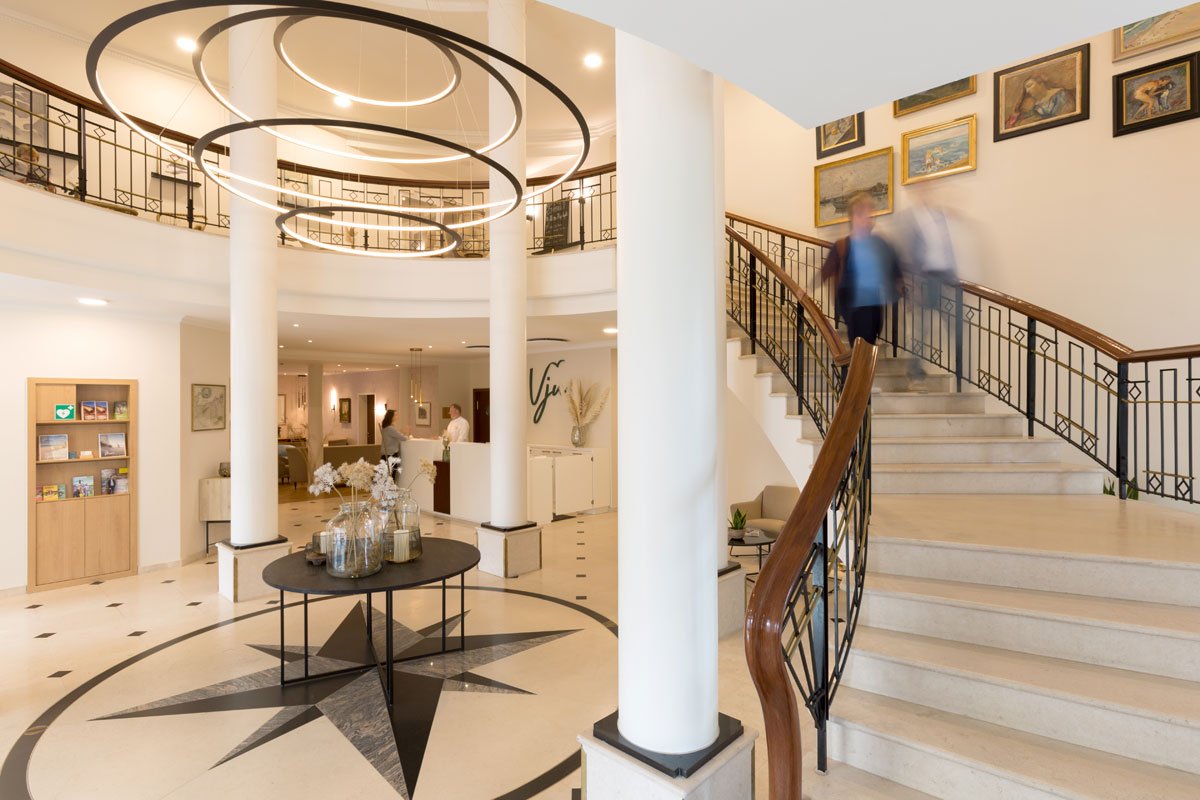 Inviting reception area with bright lobby, curved staircase and stylish chandeliers at the Vju Hotel on Rügen.