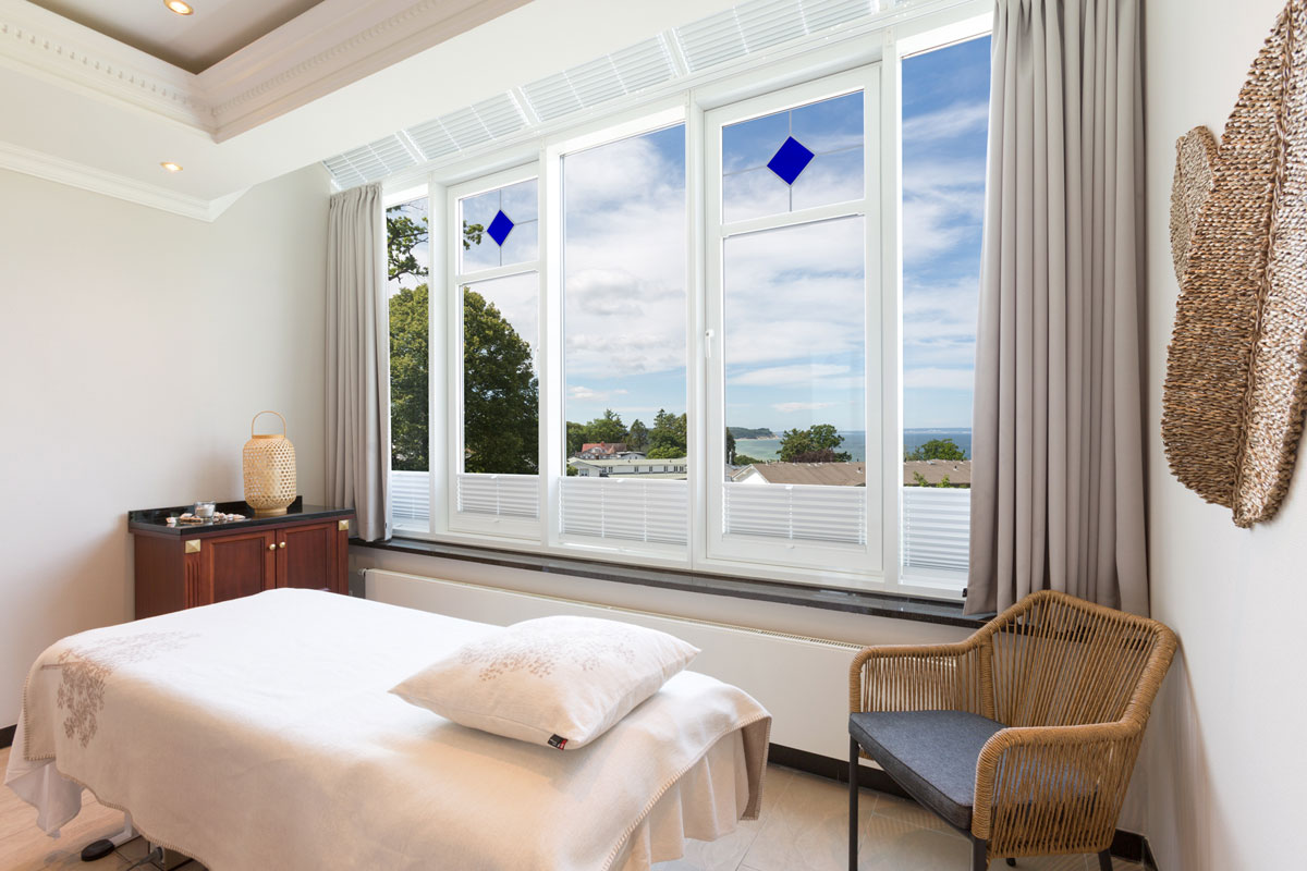 Bright massage room with large window front, comfortable lounger and sea view in the wellness area of the Vju Hotel.