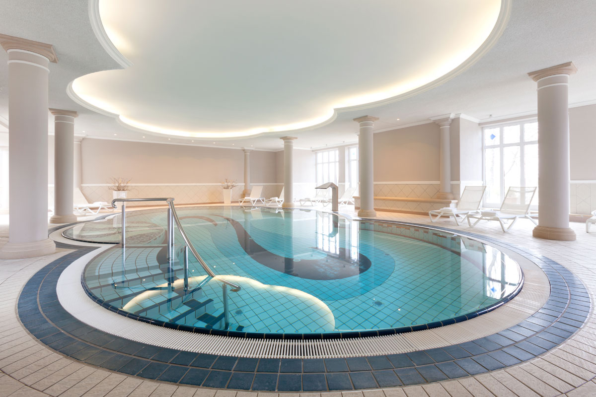 A stylish indoor pool with curved shapes and elegant columns in the wellness area of the Vju Hotel on Rügen.