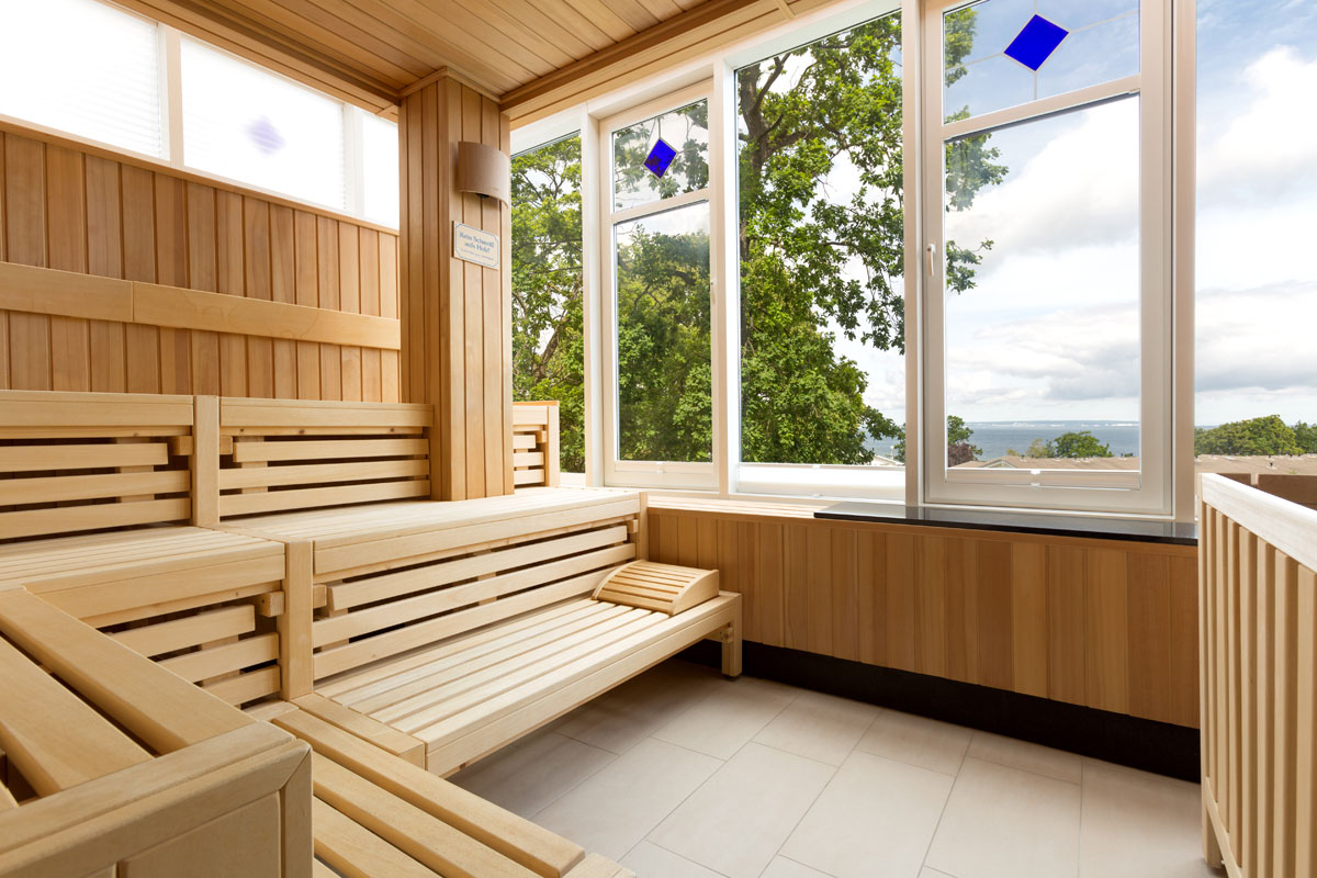 Bright wooden sauna with benches, large windows and a view of the Baltic Sea and green nature in the wellness area of the Vju Hotel.