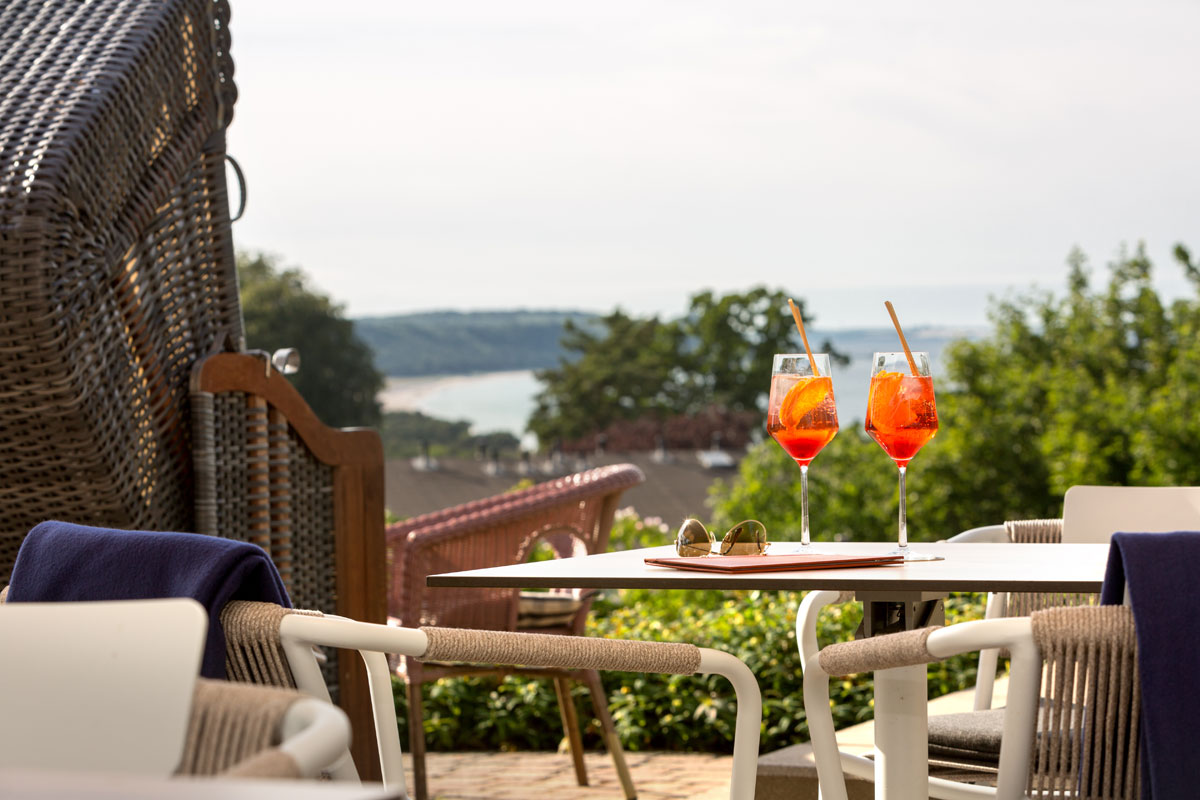 Sunny hotel terrace with rattan furniture, aperitif glasses and wonderful views over the coast on vacation at the Vju Hotel.