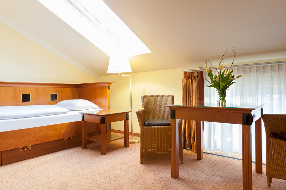 Hotel room with single bed, desk, rattan chairs and large windows in the annexes of the Vju Hotel.