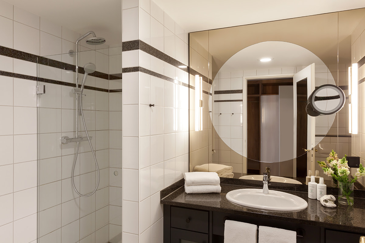 Modernes Badezimmer mit großer Dusche und beleuchtetem Spiegel in der 2-Raum Familiensuite im Vju Hotel auf Rügen.