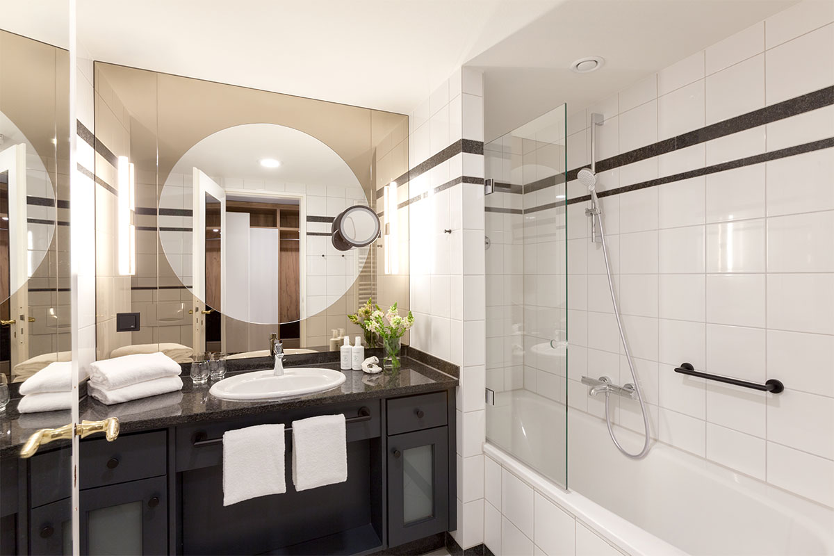 Modern hotel bathroom with a large mirror surface, sink, towels and bathtub in the single room of the Vju Hotel.