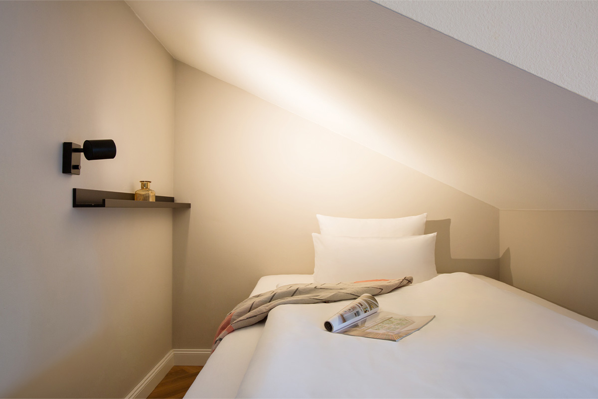Cozy single bed under a sloping ceiling in the queen-size single room of the Vju Hotel.
